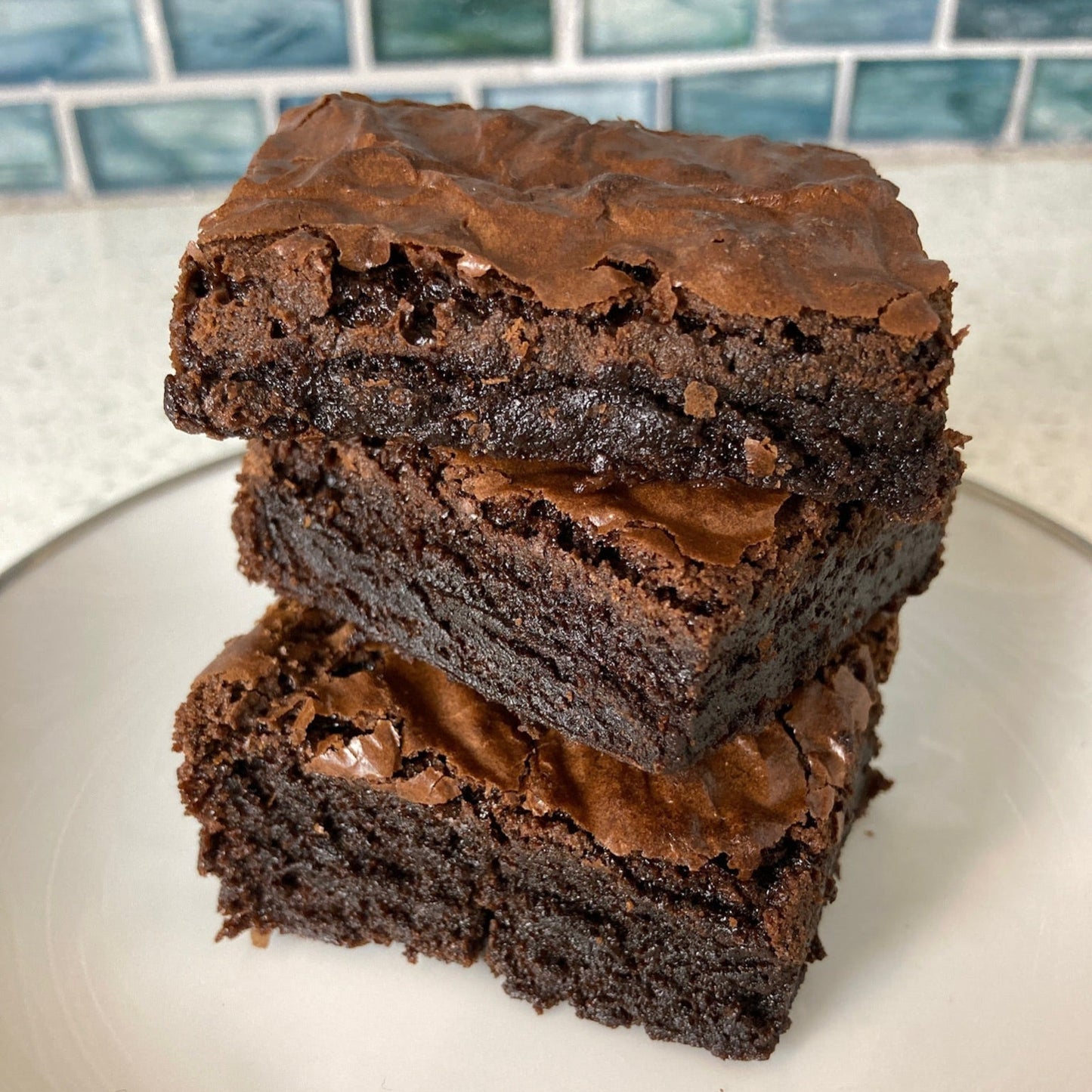 Stack of brownies on a white plate with a tiled backsplash in the background