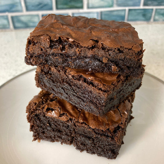 Stack of brownies on a white plate with a tiled backsplash in the background